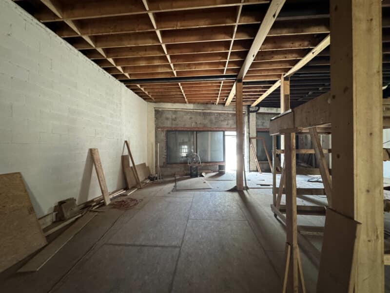 Unfinished commercial interior with exposed ceiling joists, wood framing, and plywood flooring.