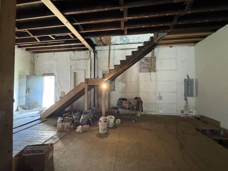 Unfinished commercial space with staircase, exposed framing, and construction materials on the floor.