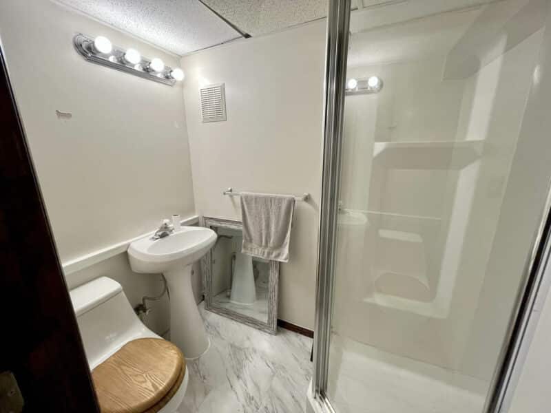 Full bathroom in basement featuring a pedestal sink, toilet with wooden seat, and corner glass-enclosed shower.
