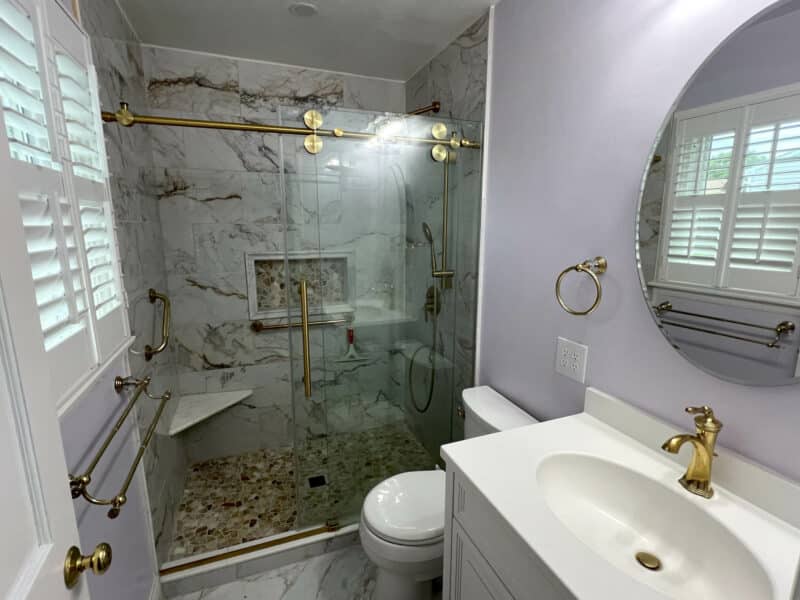 Updated bathroom with marble tile shower, glass enclosure, and gold fixtures in Dundalk home.