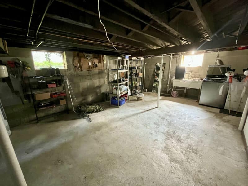 Unfinished basement room with concrete flooring, open ceiling joists, and utility shelving.