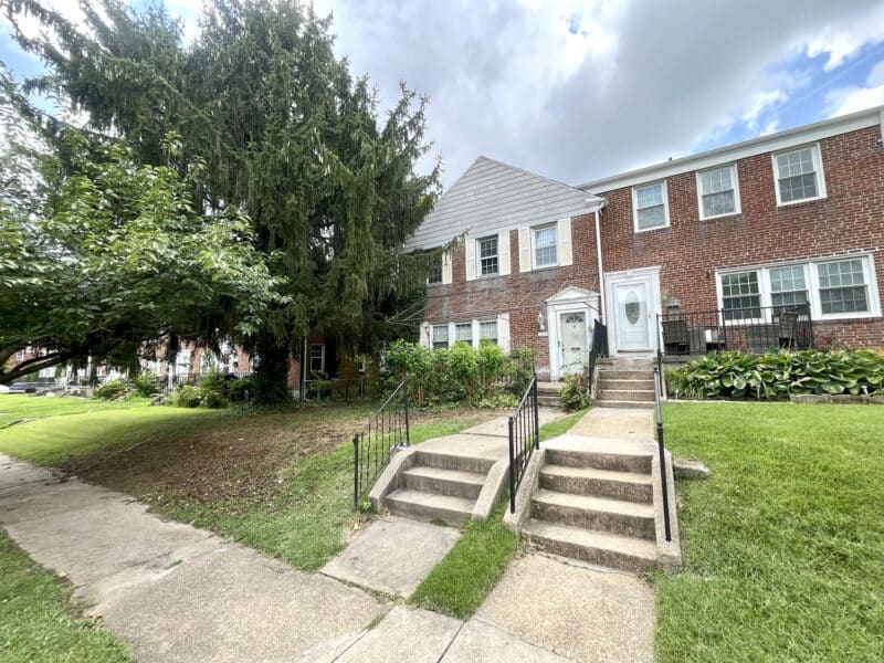 Front exterior view of a two-story brick end-of-group townhome with a concrete staircase and mature landscaping.