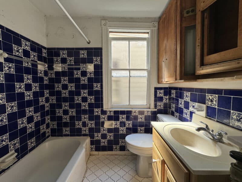 Second-floor full bathroom with bold blue and white tile, bathtub, vanity, and window.