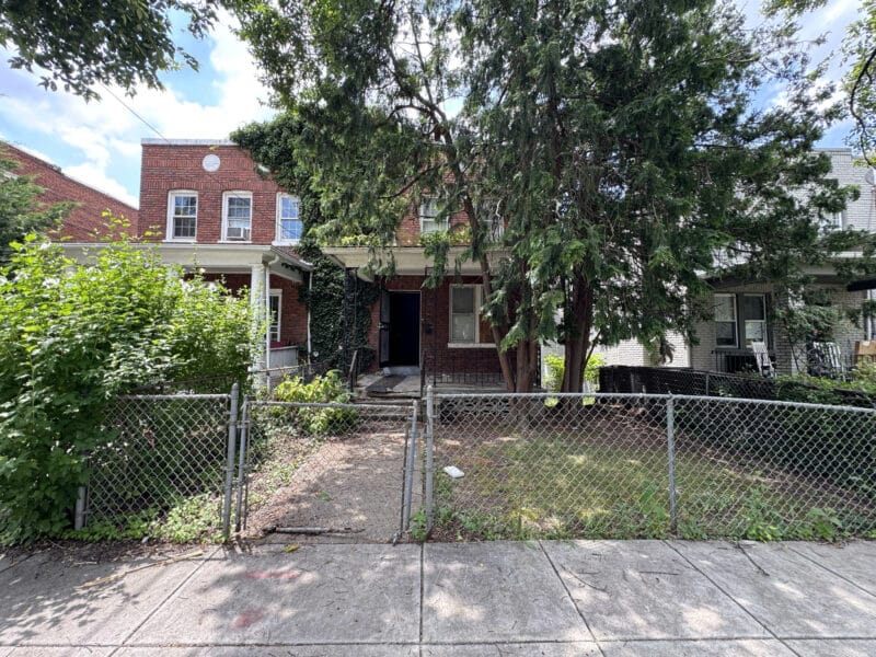 Front exterior of 909 Jackson Street NE, a brick semi-detached townhome with fenced yard and mature trees.