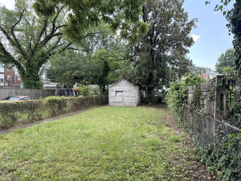 Rear yard of 909 Jackson Street NE with grassy lawn, chain-link fencing, and detached garage.