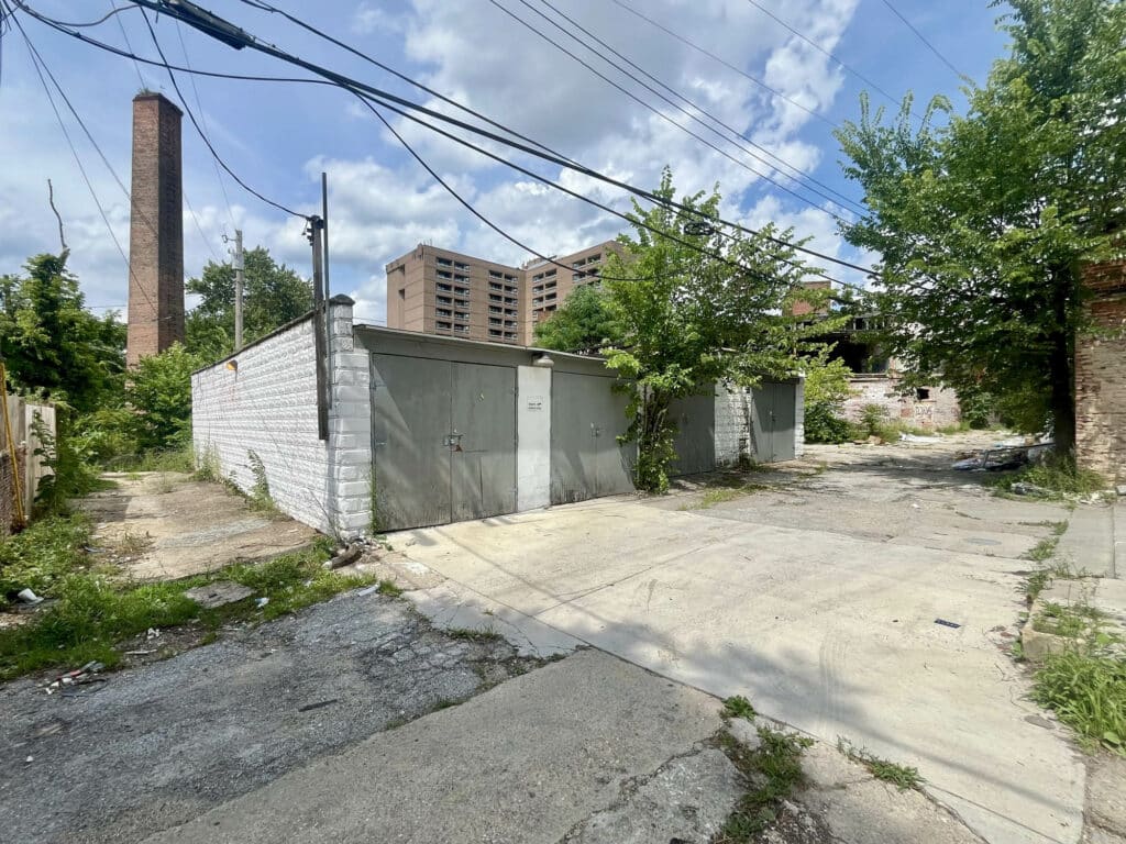 Front and side view of a concrete block garage building with four oversized wood doors.