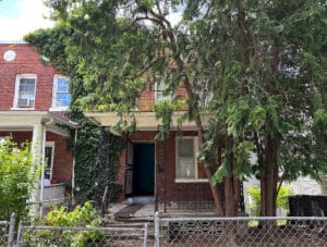 Front exterior of a semi-detached brick townhome at 909 Jackson Street NE in the Brookland neighborhood of Washington, DC, with a fenced yard and mature tree coverage.