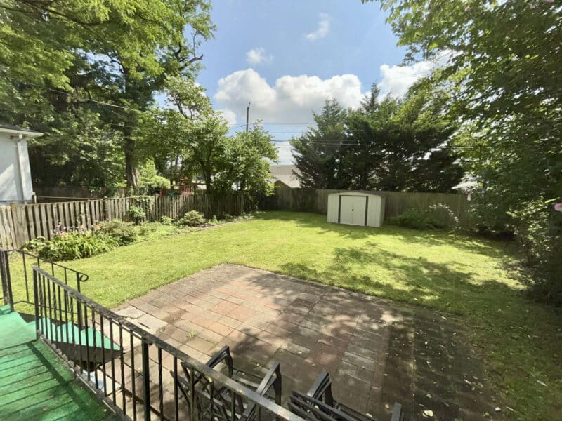 Backyard view of 19 Dunmore Road featuring a fenced yard, patio, and storage shed surrounded by mature trees.