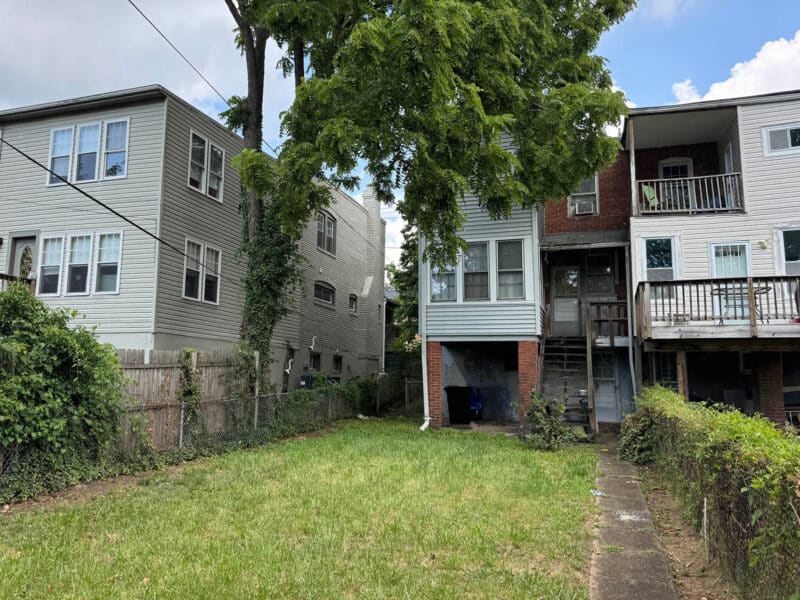 Rear view of semi-detached townhome at 909 Jackson Street NE with grassy yard, concrete path, and detached garage access.