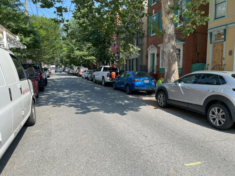 Tree-lined street view of Prince George Street in Downtown Annapolis, featuring parked cars and historic townhomes.