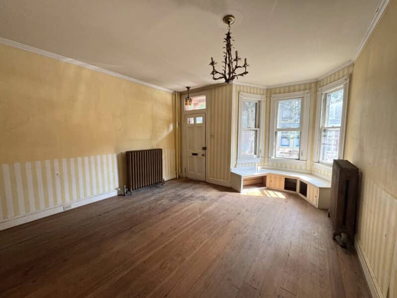 Victorian living room with wood floors, bay window, radiator, and decorative chandelier at 199 Prince George Street.