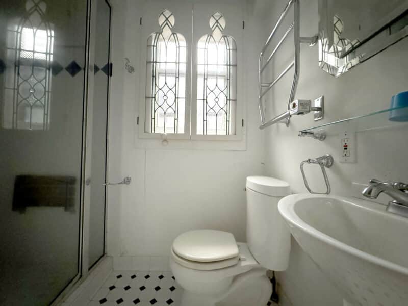 First-floor bathroom with pedestal sink, toilet, glass shower enclosure, and arched stained glass windows.