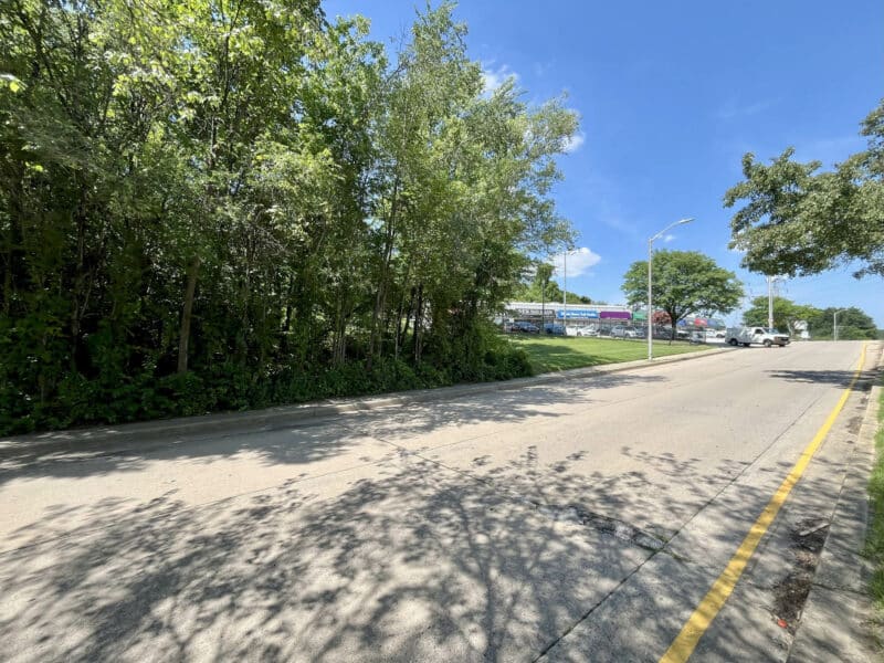 View looking along Sinclair Lane with wooded frontage and nearby commercial development in Frankford, Baltimore City.