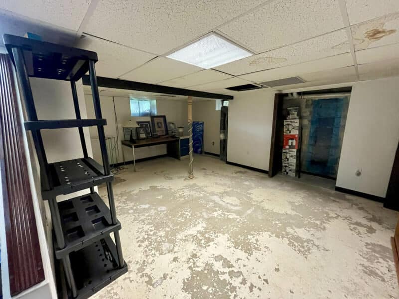 Unfinished basement room with drop ceiling, shelving units, and exposed concrete floor at 19 Dunmore Road.