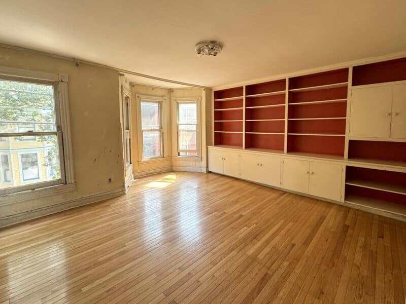 Large bedroom with hardwood flooring, bay windows, and built-in red shelving unit.