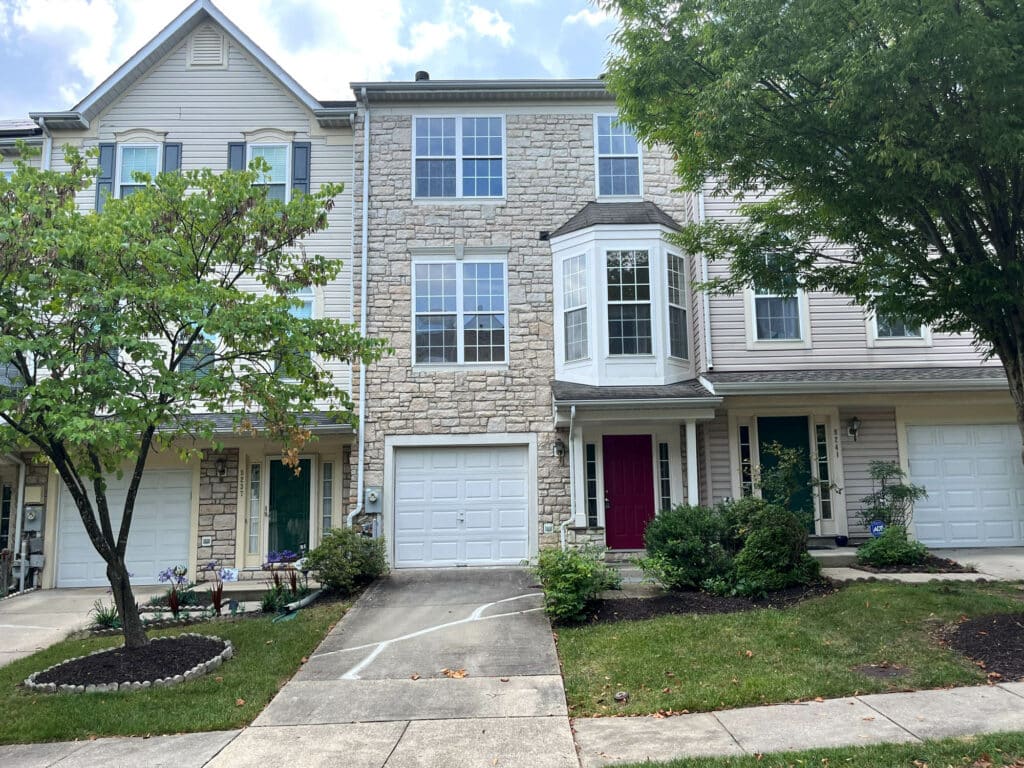 Front exterior of 8239 Brooktree Street, a three-story garage townhome with stone façade, one-car garage, and landscaped front yard in Laurel, MD.