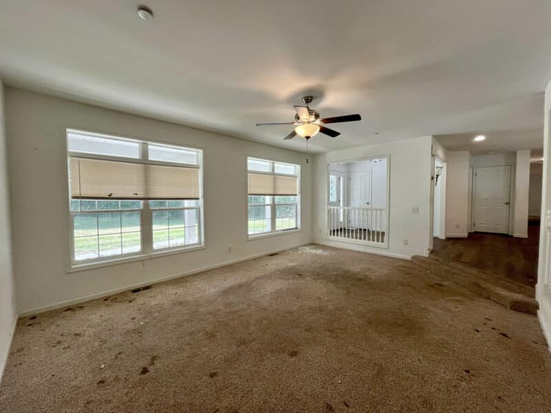 Sunken living room with carpet, ceiling fan, and large front windows.