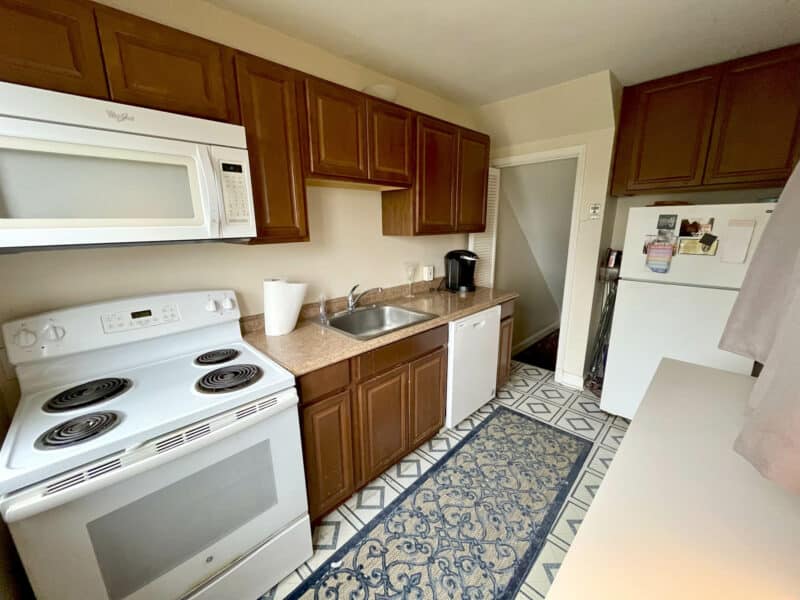 Galley-style kitchen with electric range, microwave, dishwasher, wood cabinets, and tile flooring at 1000 Downton Road in Arbutus, MD.