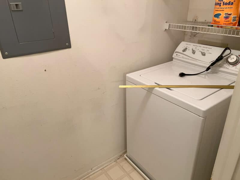 Laundry area with top-loading washer, wall-mounted shelf, and utility panel in Bel Air condo unit.