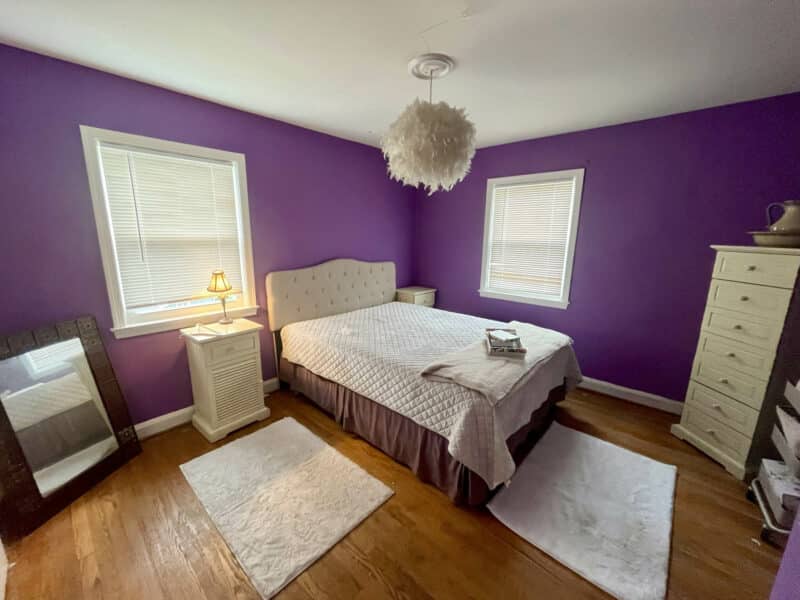 Bedroom with hardwood floors, bold purple accent walls, and a bed with white linens at 1000 Downton Road in Arbutus.