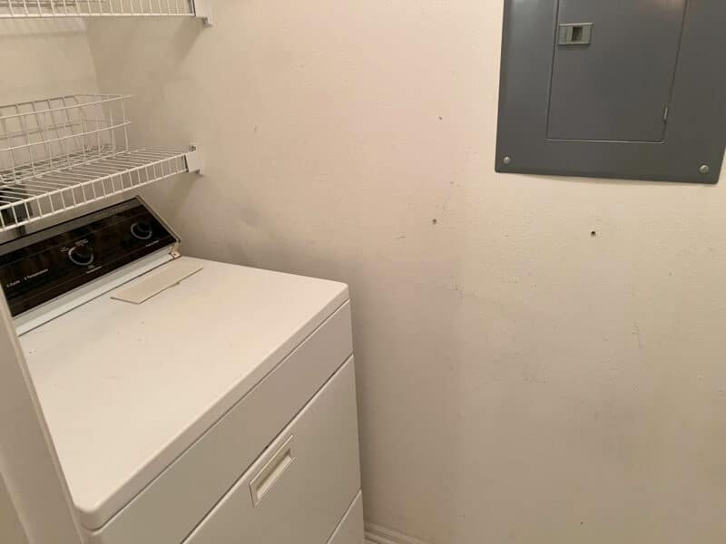 Laundry area featuring a top-loading dryer with wire shelving and nearby electrical panel.