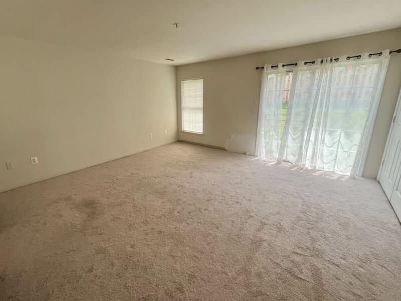Spacious living room with carpet flooring, large window, and sliding glass doors with sheer curtains at Baltimore home.