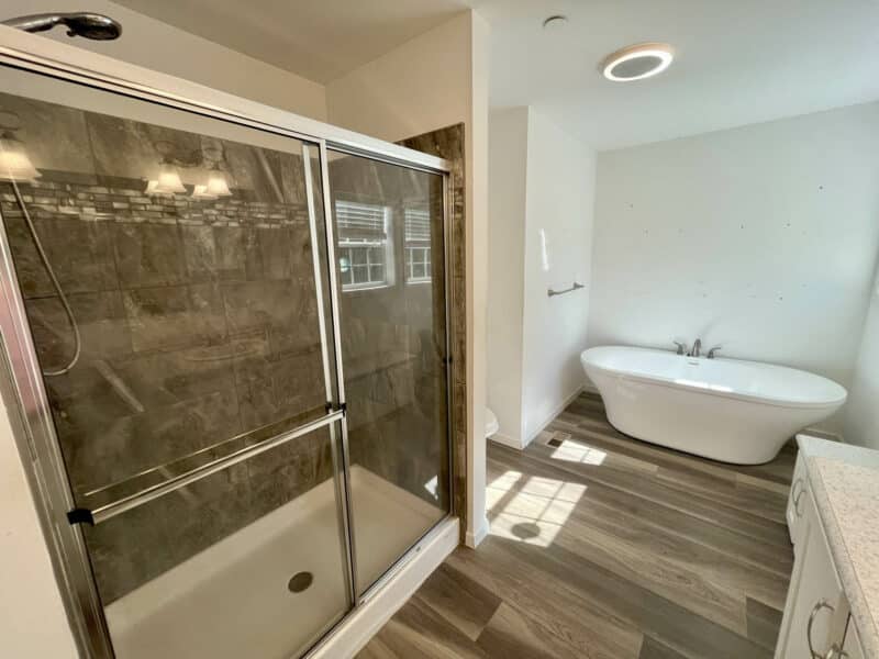 En-suite bath with walk-in shower, soaking tub, dual vanities, and wood-style flooring.