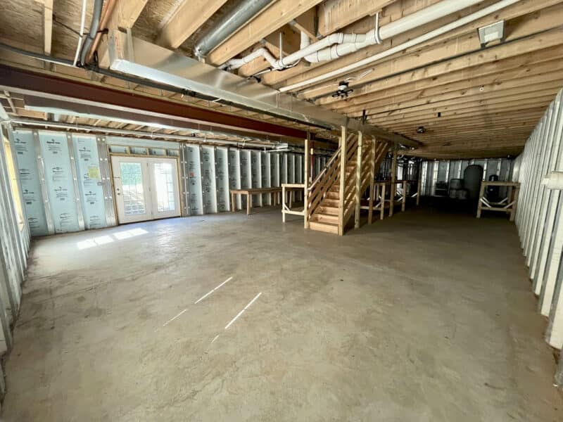 Full-height unfinished basement with framing, concrete floors, and stair access.