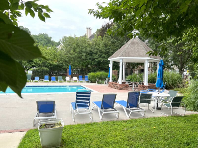 Poolside seating and shaded gazebo within a landscaped community recreation area.