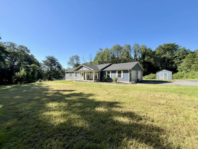 Wide-angle view of ranch home and expansive front yard surrounded by mature trees.