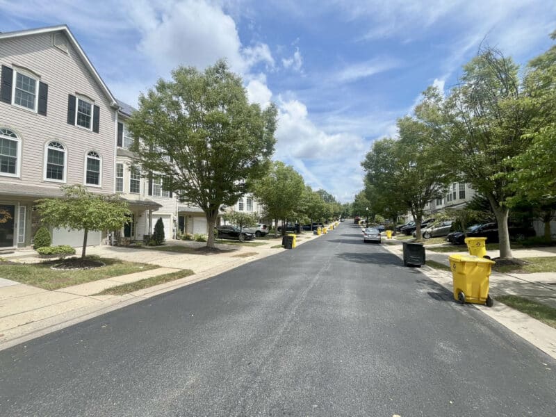 Tree-lined residential street with townhomes and fresh asphalt in a suburban neighborhood.