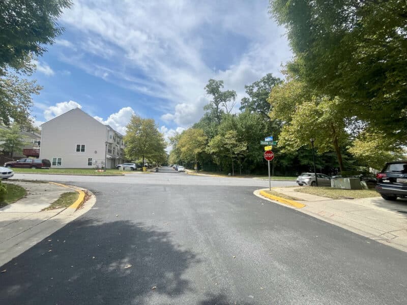 Neighborhood street corner with stop sign, trees, and residential townhomes.