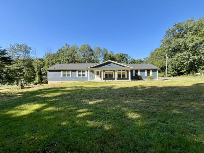 Front exterior view of a 2019 ranch-style home with blue siding, asphalt shingle roof, and covered porch, located on a 1.68-acre lot in Street, Harford County, Maryland.