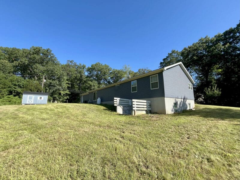 Rear angle view of 2019 ranch home in Street, Harford County, showing backyard, sloped lawn, and exterior storage shed.