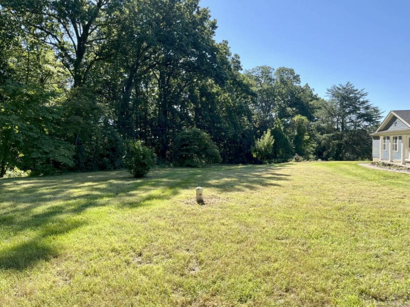 Front yard of property with open grassy area and mature trees.