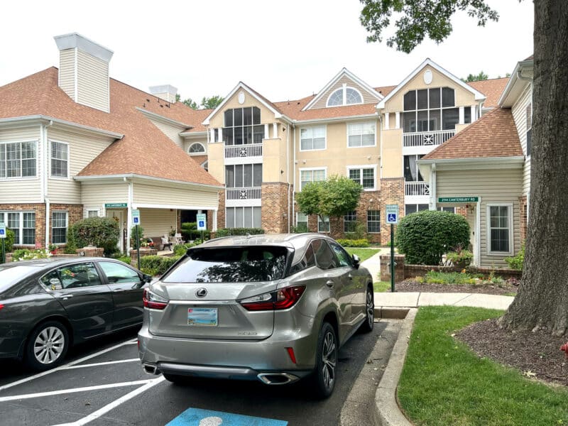 View of English Country Manor condominium complex with parked vehicles, accessible spaces, and well-maintained exterior.