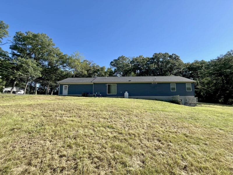 Rear view of ranch home with open yard and walk-out basement access.