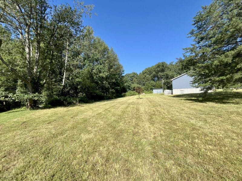 Rear side angle of property with open grass and trees in background.