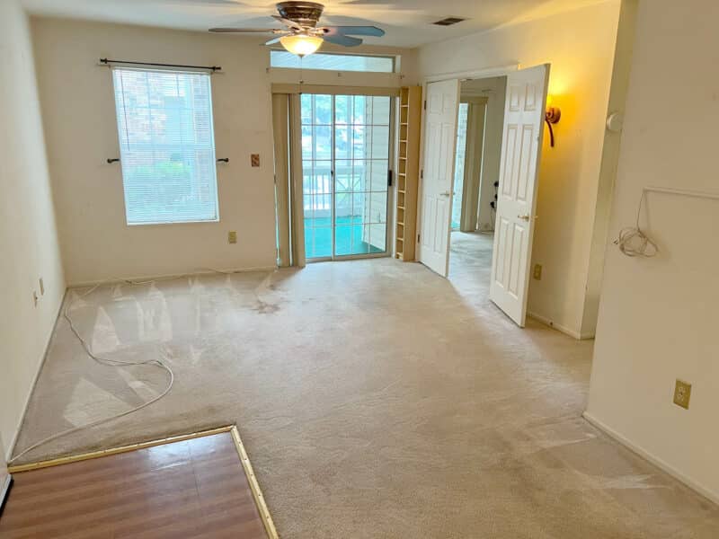 Carpeted living room with ceiling fan, sliding glass doors to screened porch, and entry to additional rooms in Bel Air condominium.