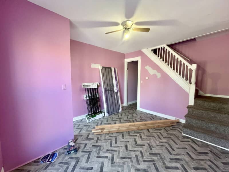 Living room of two-story Broadway East townhome with pink walls, vinyl flooring, ceiling fan, and staircase leading to the second floor.