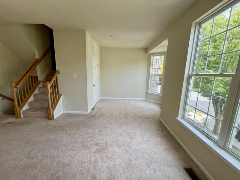 Bright living room with large window and sliding glass door, neutral walls, and carpet flooring.
