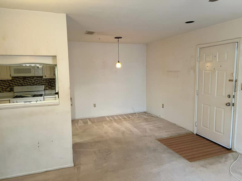 Dining area with overhead pendant light, carpet flooring, and view into kitchen through a passthrough in Bel Air condo unit.