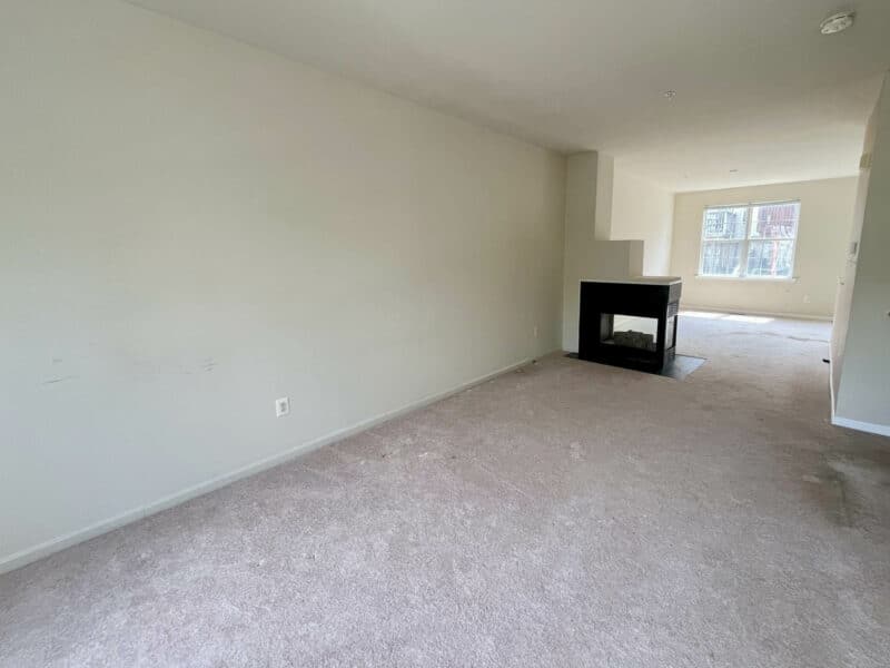 Townhouse living room with neutral carpeting, fireplace, and large window.