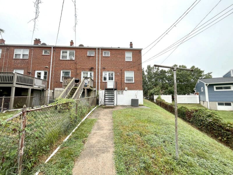 Rear exterior view of 1000 Downton Road, an end-of-group brick townhome in Arbutus with fenced backyard, rear steps, and basement walk-out.