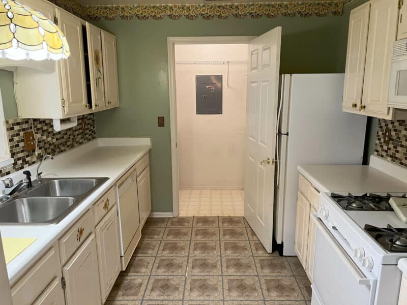 Galley-style kitchen with white cabinets, dual-basin sink, gas range, and tiled flooring in Bel Air condominium unit.