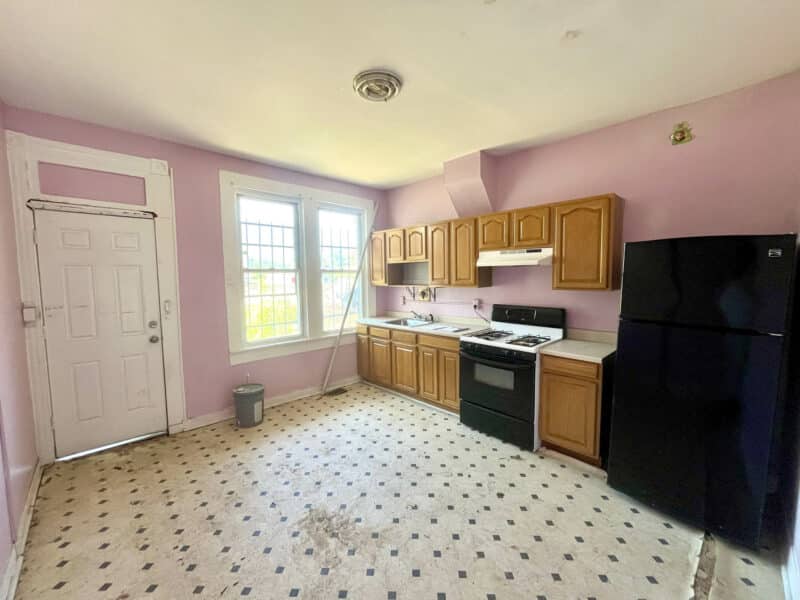 Renovation-ready kitchen in Broadway East townhome featuring wood cabinetry, vinyl flooring, and rear door access.