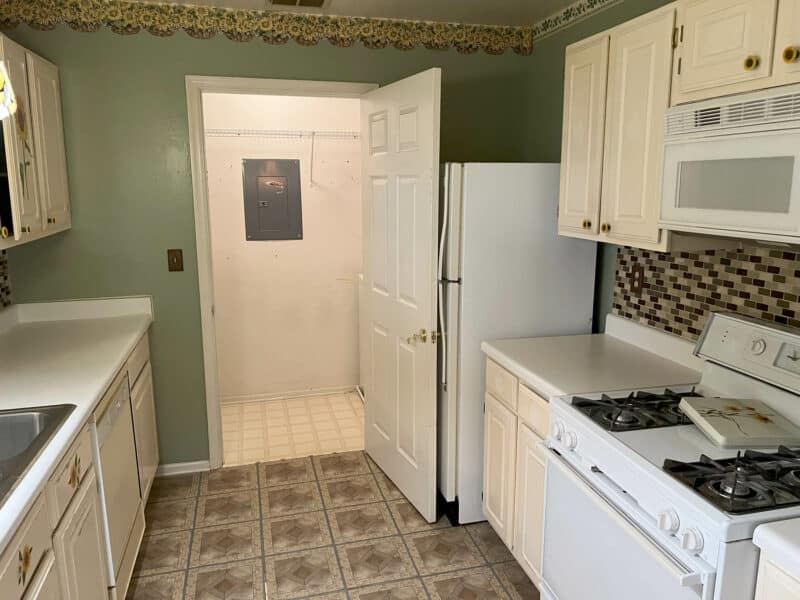 Another angle of the kitchen showing white appliances, gas stove, mosaic backsplash, and tiled flooring in Bel Air condo unit.