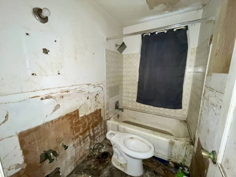 Full bathroom in need of renovation with damaged walls, toilet, and bathtub at 4902 Gilray Drive.