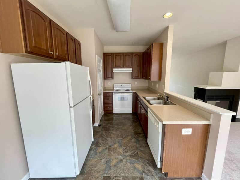 Kitchen with wood cabinetry, white appliances, and breakfast bar counter.