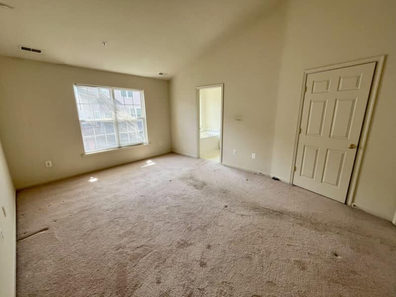 Bedroom with large window, neutral walls, and carpet flooring.